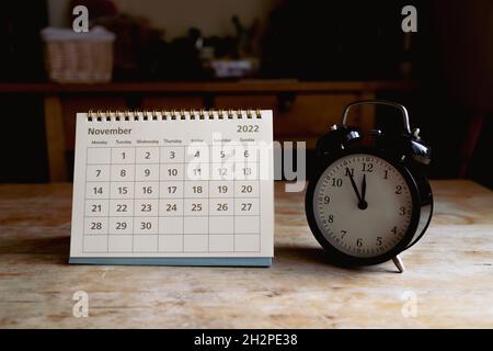 November 2022 calendar and black vintage clock on wooden table Stock Photo