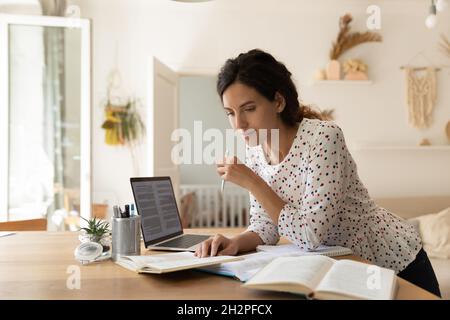 Focused adult female student doing homework, reading books at laptop Stock Photo