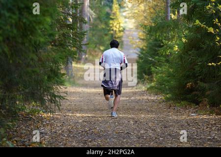 Athlete man jogging in autumn forest. Male runner training outdoors before running marathon in park Stock Photo
