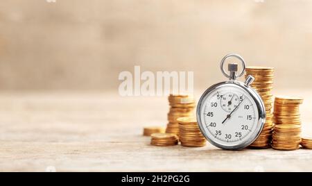 Time is money. Stopwatch and stacks of coins on a wooden background. Template Copy space for text. Stock Photo