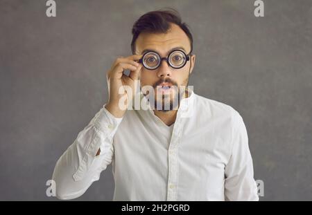 Close up portrait of shocked caucasian man in funny glasses with magnifying glass. Stock Photo