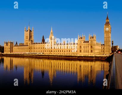 Houses of Parliament illuminated by clear sunrise reflected in the still River Thames at high tide from Westminster Bridge London UK Stock Photo