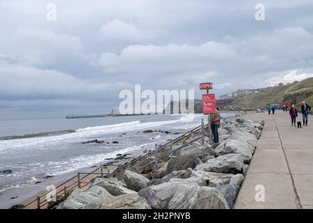 Whitby, North Yorkshire, UK – October 17 2021. Unidentifiable couple standing at the top of the steps from the promenade or esplanade to the sandy bea Stock Photo