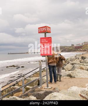 Whitby, North Yorkshire, UK – October 17 2021. Unidentifiable couple standing at the top of the steps from the promenade or esplanade to the sandy bea Stock Photo