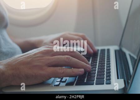 using onboard internet on laptop in airplane, passenger working on computer in  plane, closeup of hands typing on keyboard inside aircraft Stock Photo
