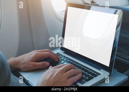 passenger using laptop computer in airplane, onboard wifi internet connection in flight, white empty screen Stock Photo