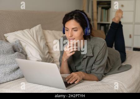 Relaxed focused female student in headphones lying on couch Stock Photo