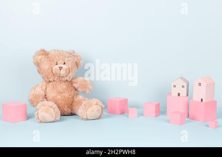 Kids toys collection. Cute teddy bear, pink wooden cubes and toy houses on light blue background. Front view Stock Photo