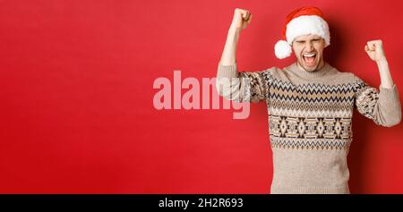 Satisfied handsome man, feeling lucky and happy, shouting for joy and making fist pumps, celebrating victory or win, receive awesome christmas gift Stock Photo