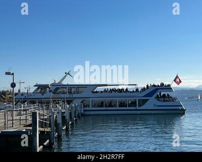 Cruise ship on lake Zurich. Ship is moored to the pier to let the passengers get on and off board. There ist Swiss flag on the vessel blowing in wind. Stock Photo