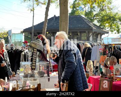 Vendor at flea market is drinking coffee from a flask. He is at his stall selling vintage and rare merchandise. Elderly man is captured in side view. Stock Photo