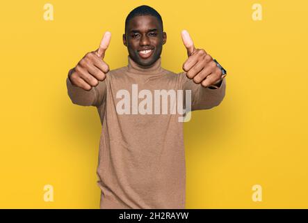Young african american man wearing casual winter sweater approving doing positive gesture with hand, thumbs up smiling and happy for success. winner g Stock Photo
