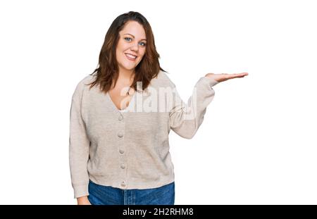 Young plus size woman wearing casual clothes smiling cheerful presenting and pointing with palm of hand looking at the camera. Stock Photo