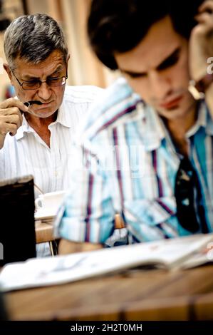 ITALY. HIGH-ADIGE. BOLZANO. MAN SMOKING HIS PIPE AND YOUNG MAN READING HIS NEWSPAPER AT A CAFE Stock Photo
