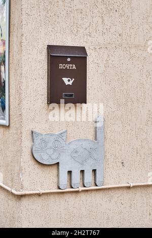 Mailbox and flat sculpture of smiling cat walking on pipe on wall with fish in its stomach. Stock Photo