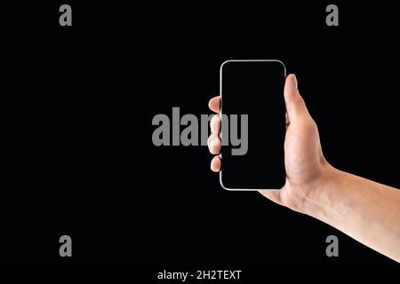 Phone and black background. Empty smartphone screen in dark. Mobile website design mockup. Hand holding cellphone to camera. Digital display. Stock Photo