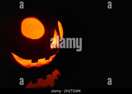 Close-up on a Jack O' Lantern lit in the dark and reflecting on a black surface in front of it. Stock Photo