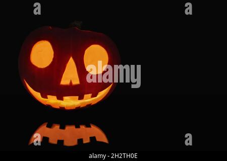 Close-up on a Jack O' Lantern lit in the dark and reflecting on a black surface in front of it. Stock Photo