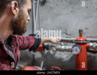 The man looks at the faucet, pipes, valve, pressure meter. Stock Photo