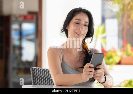 Adult woman smiling sitting in a cafe outside using phone with both hand Stock Photo
