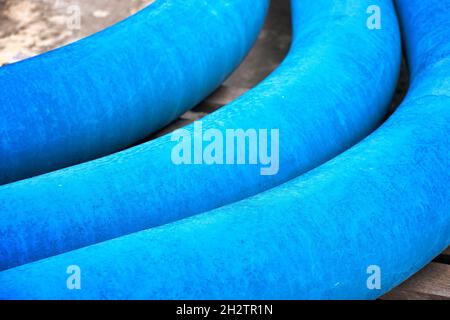Three curved blue pipes for laying the gas pipeline lie in an open warehouse on the street. Layout. Products for the construction of the gas pipeline. Stock Photo