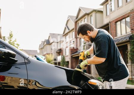 American man polishing car by polisher in front of house. Stock Photo