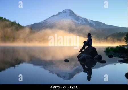 traveler sitting on rock and looking over scenic Mount Hood view with sunrise at Trillium Lake, Oregon Stock Photo