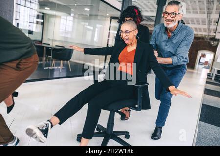 Group of businesspeople having fun during playtime. Cheerful group of colleagues pushing each other on chairs in a modern workplace. Team of businessp Stock Photo