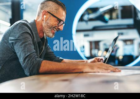 Smiling businessman attending a virtual meeting in a modern office. Experienced entrepreneur using a laptop for a video conference with his partners. Stock Photo