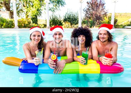 merry christmas! happy diverse group of friends portrait wearing xmas santa hat having drinks in swimming pool party celebrating winter festivities Stock Photo