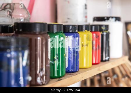 Colored paints for drawing and painting in cans on a shelf in a workshop. Stock Photo