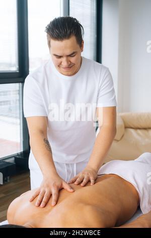 https://l450v.alamy.com/450v/2h2wbce/vertical-portrait-of-professional-male-masseur-with-strong-tattooed-hands-massaging-back-of-unrecognizable-muscular-sportsman-lying-on-stomach-2h2wbce.jpg