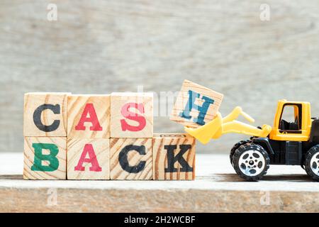 Toy bulldozer hold letter block H, K in word cash backon wood background Stock Photo
