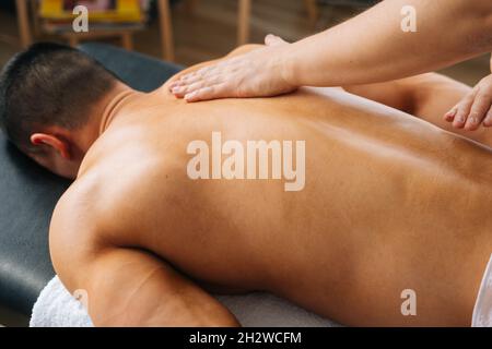 Close-up top view of unrecognizable male masseur massaging back of muscular sportsman lying on massage table. Stock Photo