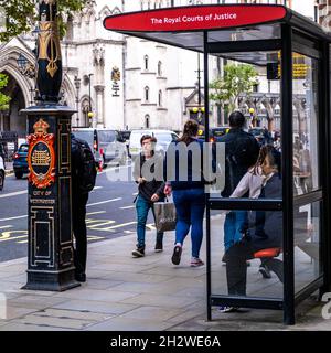 People Walking By A Woman Sitting At A Bus Shelter In The Strand Opposite The Royal Courts Of Justice In London England UK Stock Photo