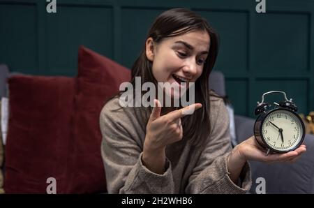 Black retro alarm clock in female hands on a blurred background. Stock Photo