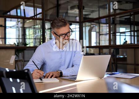 Mature business man manager looking at laptop watching online webinar in office. Stock Photo
