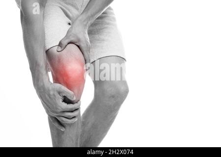 Cropped young european man suffering from knee pain, presses hand to sore spot, highlighted in red, monochrome Stock Photo