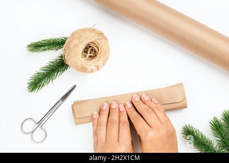 top view of woman hands wrapping Christmas gift in craft paper and jute rope on white isolated background Stock Photo