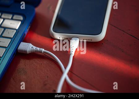 The smartphone is connected to the laptop via USB cable. Stock Photo