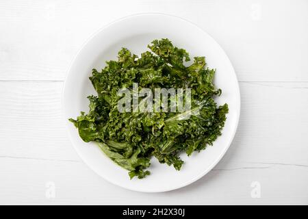Heap of oven baked crunchy curly kale chips in bowl also known as leaf cabbage. Healthy tasty vegan snack concept.