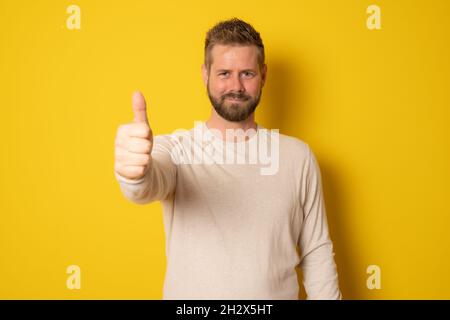 Young hipster man with thumb up isolated over yellow background. Stock Photo