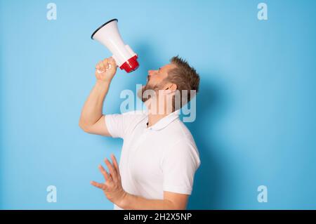 Handsome man over isolated blue wall shouting through a megaphone Stock Photo