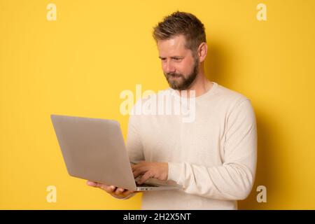 Young handsome man using laptop isolated over yellow background. Stock Photo