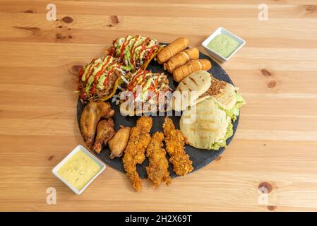 Tray of assorted appetizers, arepas, patacon with shredded meat, cheese-filled tequeños, chicken wings, battered chicken strips and dipping sauces Stock Photo