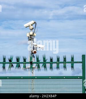 Bank of security cameras and fence with rotating spikes guarding an enclosed site in the UK Stock Photo