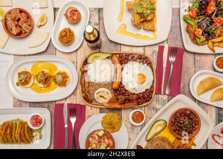 set of delicious Colombian food recipes on wooden table with paisa tray, patacones, chicharrones, fried yucca with guacamole, prawn cocktail and corn Stock Photo