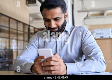 Happy indian business man using app on cell phone working in office. Stock Photo