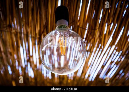 Modern energy saving filament led bulb edison style light lamp in a country tropical house with a thatched roof, modern technology, ecology concept. Stock Photo