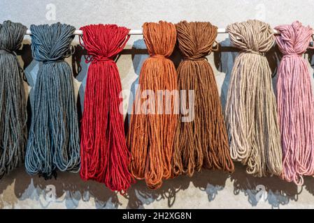 Skeins of different colored wool displayed hanging outdoors on a rod against a wall in a wool production and handicraft concept Stock Photo